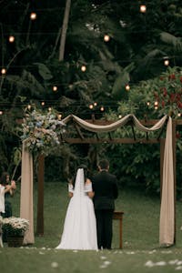 A couple getting married under a beautifully decorated arch in a garden.
