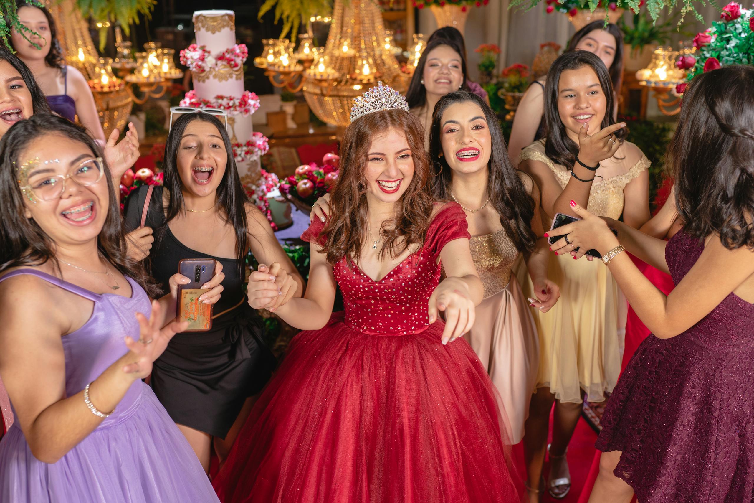 A group of young women in formal dresses delight in a festive party setting.