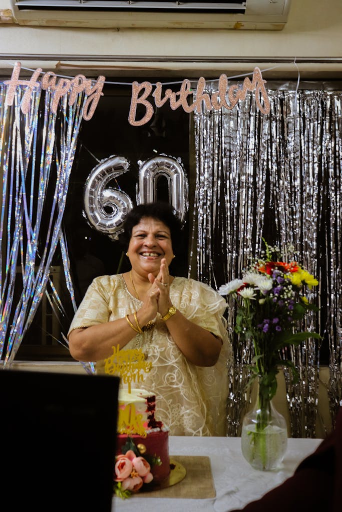A joyful woman celebrates her 60th birthday with flowers and cake indoors.